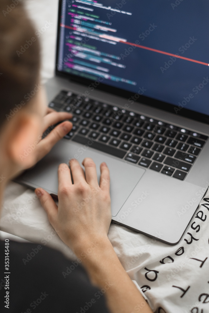 Wall mural young female programmer writes program code on a computer laptop in the bed at home. remote work