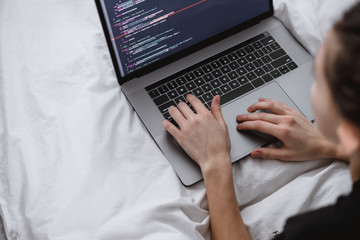 Young female programmer writes program code on a computer laptop in the bed at home. remote work