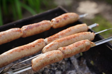 Close up of toasted sausages on skewers. Succulent kupaty roasting on chargrill. Concept of picnic outdoor.