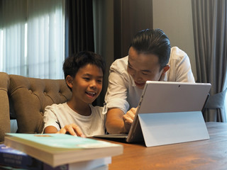 Fototapeta premium Closeup of Asian father and son working on laptop together at home.