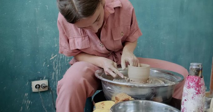 Female potter sitting and makes a cup on the pottery wheel. Woman making ceramic item. Pottery working, handmade and creative skills