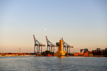 Fototapeta na wymiar The cranes in the port of Odessa at sunset with the moon in the background.