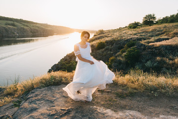 Bride in a luxurious white wedding dress in nature at sunset