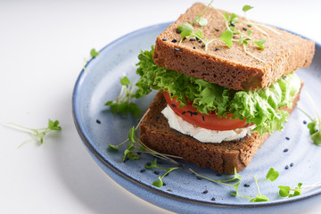 healthy sandwich with gluten-free bread, tomato, lettuce and germinated microgreens, sprinkled with...