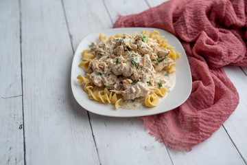 Crack chicken slow cooked dish over egg  pasta on a white plate 