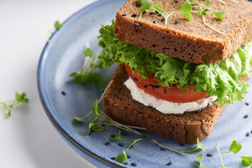 healthy sandwich with gluten-free bread, tomato, lettuce and germinated microgreens, sprinkled with sesame seeds served in plate
