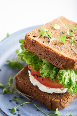 healthy sandwich with gluten-free bread, tomato, lettuce and germinated microgreens, sprinkled with sesame seeds served in plate