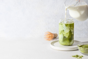 Iced Green matcha latte tea and pouring milk in glass on white background.Close up. Horizontal orientation.