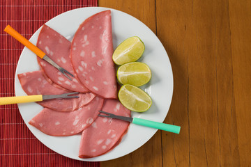 slices of mortadella served with lemon on a white plate, on a wooden background. top view
