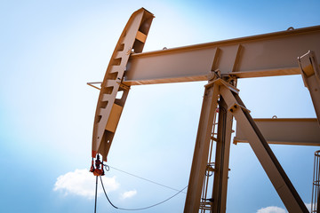 Oil beam pump or Donkey pump which is use to increase crude oil production from downhole, photo taken with blue sky background. Oil and gas industry or business photo.