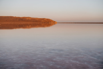 Pink salt lake at sunset. Water surface reflects the mountain.