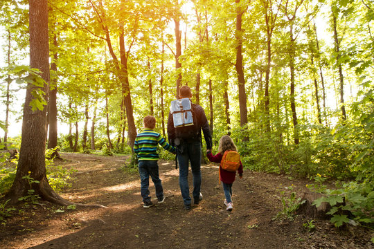 father and two kids with backpack hiking in forest. Social Distancing. Digital detox. Staycations, hyper-local travel,  family outing, getaway, natural environment