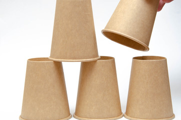 Brown paper cup for coffee, tea, a drink from environmental materials on a white background. The male hand builds a pyramid of cups in macro and overall plan. Place for text on the left and right.