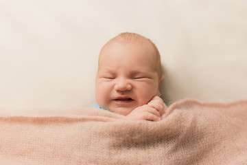newborn baby grimaces on his face. emotional newborn on a beige background