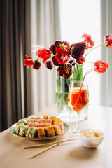 Beautiful sushi on the table, with an orange cocktail and a bouquet of tulips