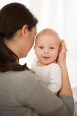 Portrait of happy mother and baby, parent and little kid relaxing at home. Family having fun together.
