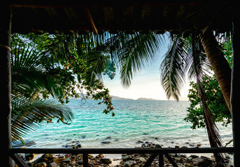 Front view on the wooden terrace in the morning is beautiful seascape. There have clear skies and many coconut trees. And Blue ocean, white sand beaches, and numerous rocks. Peaceful holiday concept.