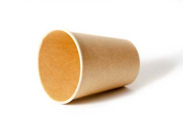 Brown paper cup for coffee, tea, a drink from environmental materials on a white background. One paper cup lies on its side and a shadow falls from it. glass with a neck sideways on a gray background