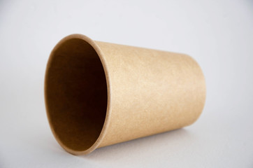 Brown paper cup for coffee, tea, a drink from environmental materials on a white background. One paper cup lies on its side and a shadow falls from it. glass with a neck sideways on a gray background