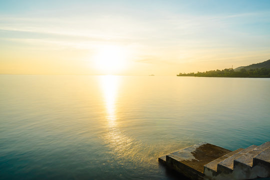The sunrise on blue ocean in the morning. There is reflection on the still water with warm light. The old gray cement stairway stretches into the sea. Feeling fresh and relaxing. there is copy space.