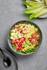 Cobb Salad in gray matte bowl on concrete backdrop. American cuisine dish with tomatoes, chicken, bacon, eggs, cheese, avocado and romaine lettuce. USA food and meal