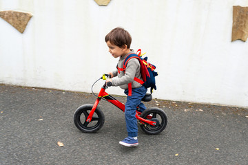 Fototapeta na wymiar Little boy rides his red balance bike on a pavement, with some motion blur