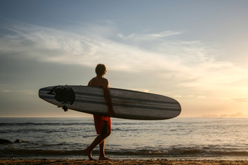 Surfer carrying his surfboard during sunset on the beach