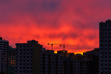Fototapeta na wymiar two construction cranes rise above residential buildings under construction against a bright beautiful sunset sky