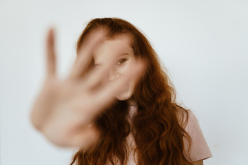 Fototapeta premium cheerfully smiling red-haired disheveled girl closes the camera with a palm with spread fingers