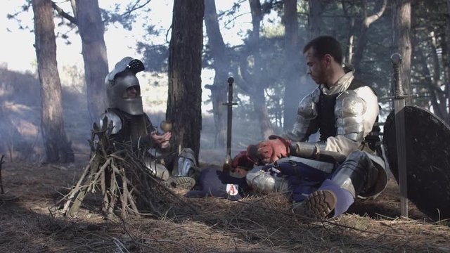 Two medieval knights sitting near bonfire and devide production