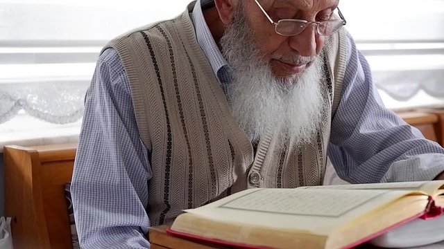 Close-up of an Elderly Muslim Turkish Man's face who is reading Holy Quran during Ramadan. Grandfather with glasses and white beard reading holy book. Selective  Focus.