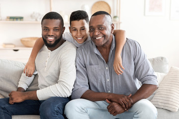 African boy hugging father and grandpa while posing to camera at home