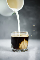 Milk is poured into a glass with coffee.