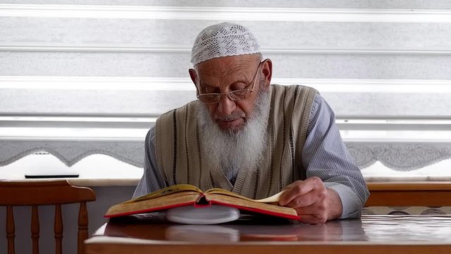 Close-up of an Elderly Muslim Turkish Man's face who is reading Holy Quran during Ramadan. Grandfather with glasses and white beard reading holy book. Selective  Focus.