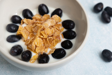 Close up a bowl of fresh grapes and yogurt with cornflakes served on a light blue background