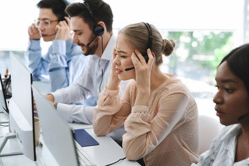 Busy call centre assistants with headsets working in front of computer monitors in open space office