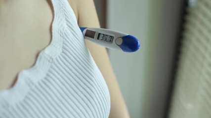 The girl turns on the electronic thermometer and inserts it into the armpit. Body temperature measurement. Close up