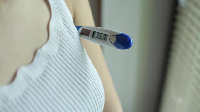 The girl turns on the electronic thermometer and inserts it into the armpit. Body temperature measurement. Close up