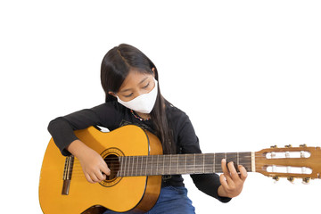 An Asian schoolgirl wearing a mask and playing the guitar at home.The picture shows the idea during home quarantine to reduce the spread of the corona virus.