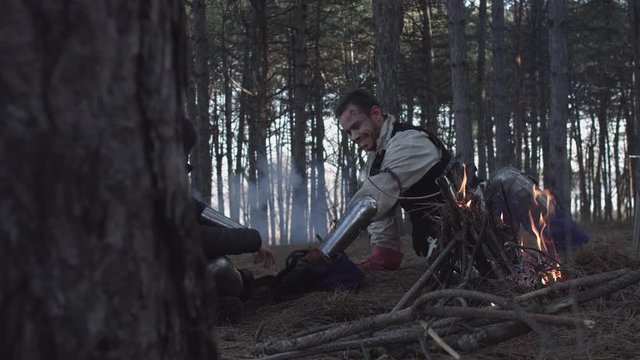 Two medieval knights sitting near bonfire and devide production