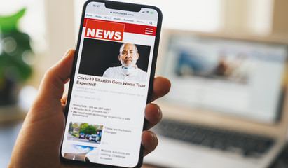 Close up of businessman reading news or articles in a mobile phone screen app. Hand holding smart device. Mockup website. Newspaper and portal on internet. Displayed news are not reality related.