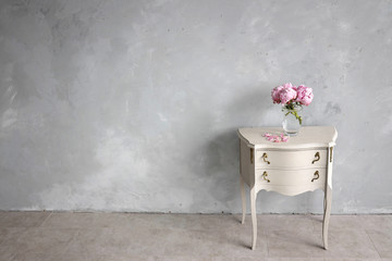 Vintage nightstand in the loft interior. Minimalistic background, copy space. A glass vase with Dutch peonies on a gray nightstand.