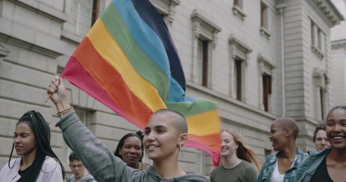 Happy young people with rainbow flag attending a gay parade. Group of men and women participating in gay pride march.
