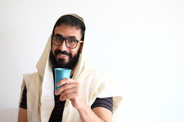 Bearded Jewish with a  Tallit (talis) and holding a cup of wine for the Kidush. The man is standing...