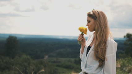 Girl with natural appearance in a white shirt collects dandelions in a field in summer