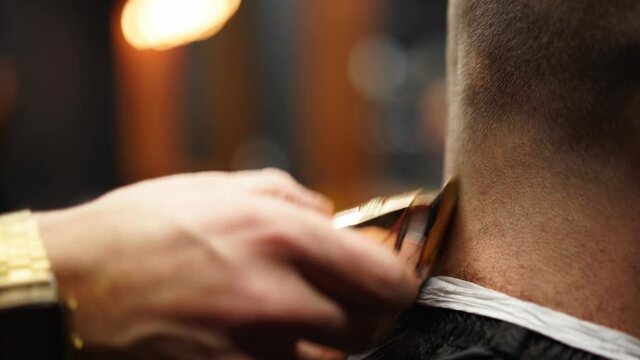 Trendy barber cuts bearded man's hair with a clipper in barbershop. Men's hairstyling and hair cutting in salon. Grooming the hair with trimmer. Hairdresser doing haircut in retro hair salon.