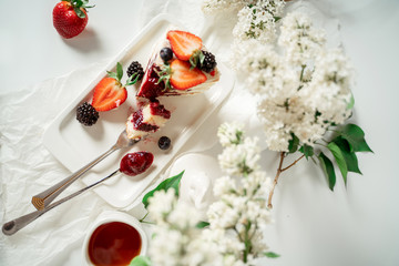 Sliced white berry cream cake decorated with strawberries and blackberries, among lilac flowers and green leaves. Food photography. Advertising and commercial close up design.