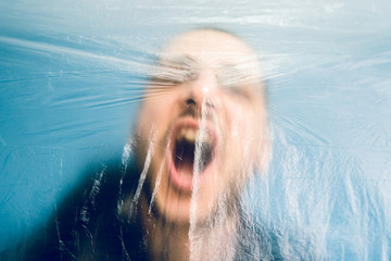 Portrait of adult caucasian man young male behind the plastic cellophane foil wrap screaming...