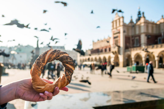Woman holding bagel / obwarzanek / pretzel - traditional Polish snack on Market Square in Cracow. .Tourist hand holding pretzel on the Cracow Cloth Hall background.