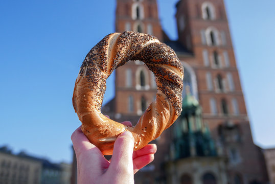 Holding bagel / obwarzanek, traditional polish snack on the Mariacka Tower background.